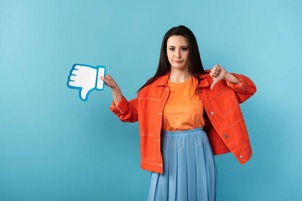 disappointed woman showing thumb down and holding paper dislike on blue background 