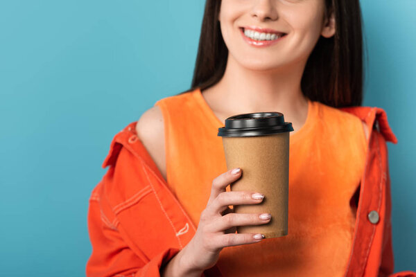cropped view of smiling woman holding paper cup with coffee on blue background 