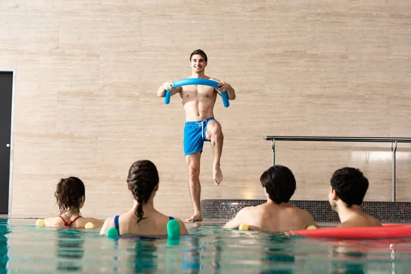 在游泳池里对一组人进行游泳池面条训练的微笑训练员的选择重点 — 图库照片