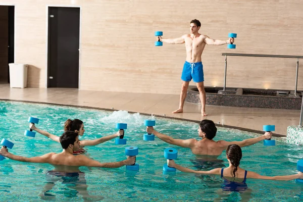 一组人和教练带哑铃在游泳池中锻炼的选择性焦点 — 图库照片