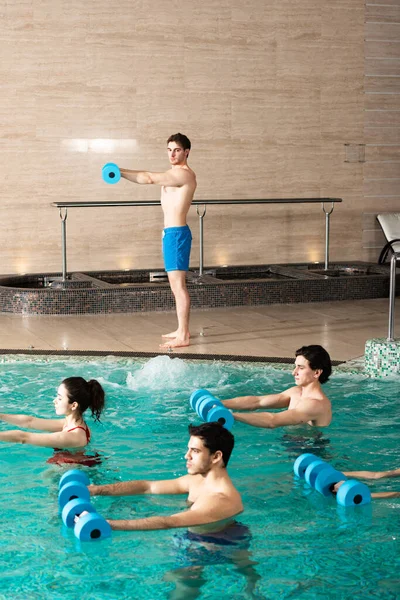 在游泳池与一群年轻人一起运动时 训练者手持哑铃的侧视图 — 图库照片