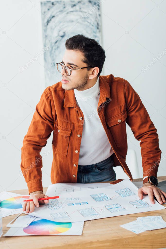 Handsome ux designer looking away while working with website templates on table