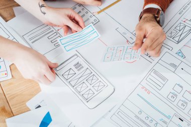Cropped view of ux designers planning interface of mobile website with layouts on table clipart