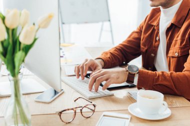 Yapımcının sofranın üzerinde x- Design ve Coffee şablonlarının yakınındaki bilgisayarı kullanmasının kırpılmış görünümü