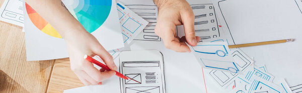 Cropped view of designers planning user experience design with layouts on table, panoramic shot