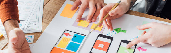 Cropped view of designers creative user experience design of mobile website with layouts on table, panoramic shot