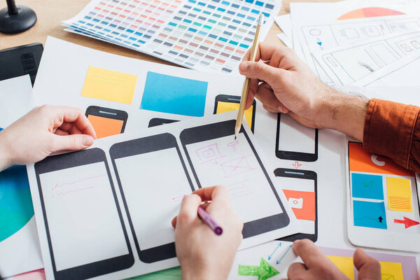 Cropped view of creative designers using mobile frameworks for user experience design of website on table