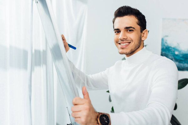 Smiling designer looking at camera while using whiteboard in office 