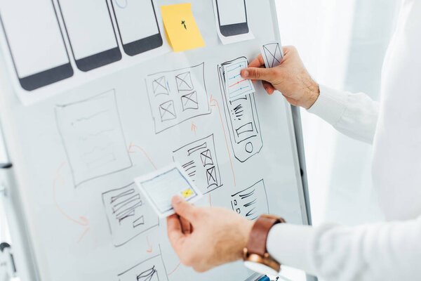 Cropped view of ux designer using layouts while creative app interface on whiteboard