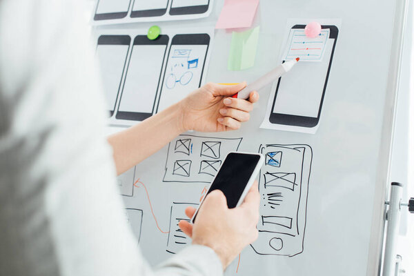 Selective focus of designers using wireframe layouts on whiteboard and smartphone while working on ux design isolated on white