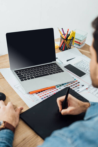 Selective focus of developer using laptop and graphics tablet near sketches of user experience design and smartphone on table isolated on grey