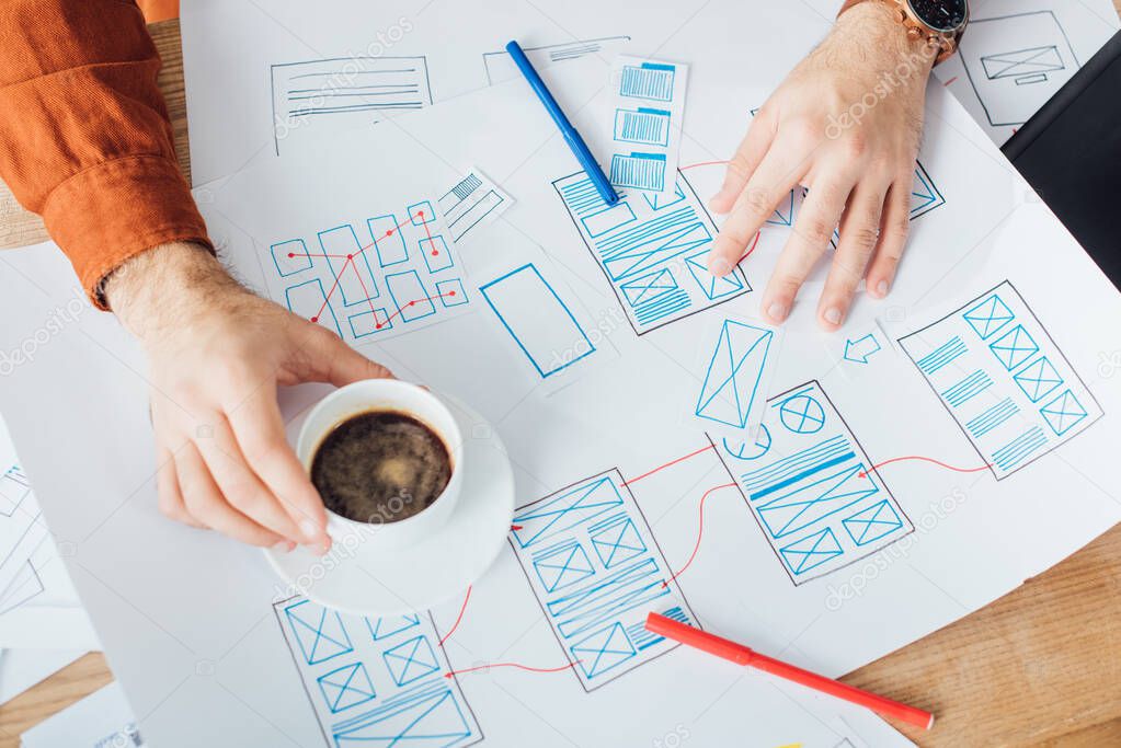 Cropped view of developer working with ux website templates and holding coffee cup on table