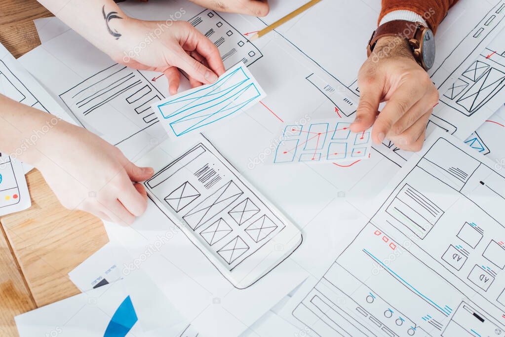 Cropped view of ux designers planning interface of mobile website with layouts on table