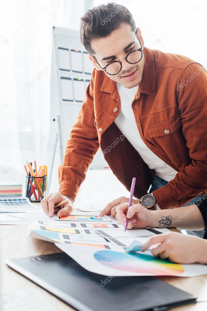 Designer looking at colleague with framework layouts of user experience design on table