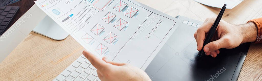 Cropped view of designer planning user experience design of website and using graphics tablet at table, panoramic shot