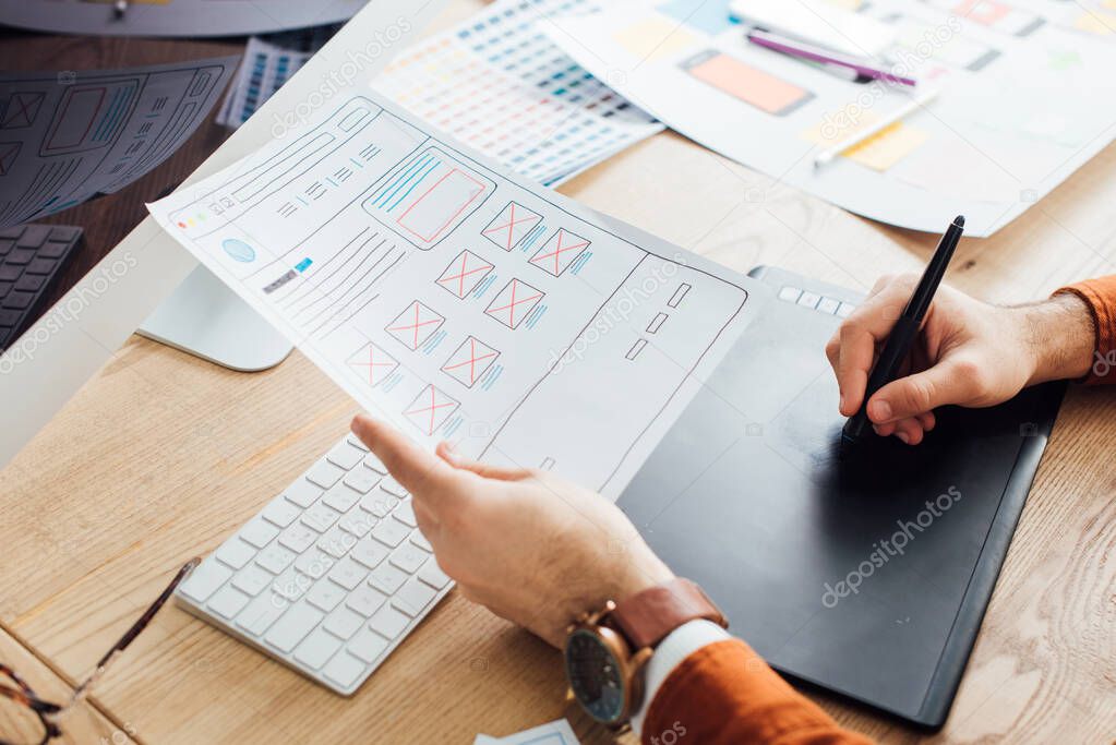 Cropped view of designer planning ux interface of website and using graphics tablet and laptop on table