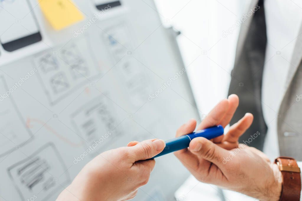 Cropped view of ux designer giving marker to colleague near project of ux design on whiteboard on white background