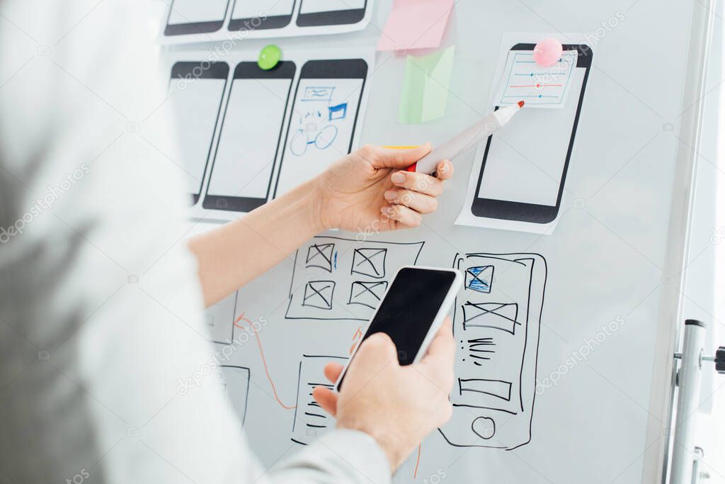 Selective focus of designers using wireframe layouts on whiteboard and smartphone while working on ux design isolated on white