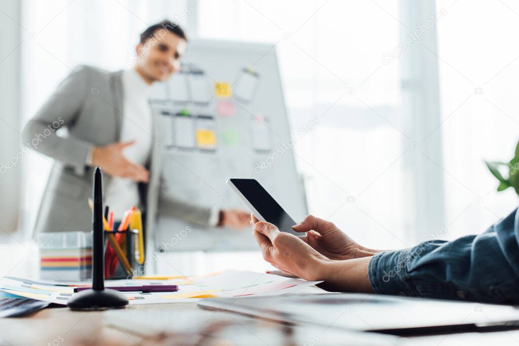 Selective focus of ux designer looking at colleague near whiteboard with layouts in office