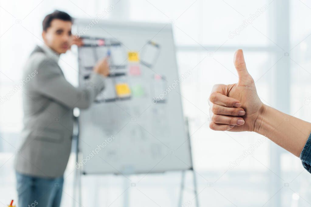 Selective focus of ux designer showing like sign to developer near whiteboard in office 