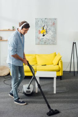 Evde elektrikli süpürgeyle halı temizleyen kulaklıklı adam. 