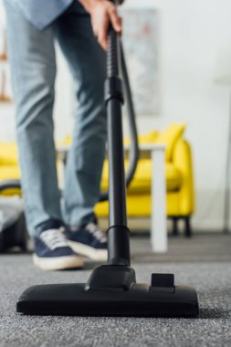 Oturma odasında elektrikli süpürge kullanan bir adamın seçici odağı
