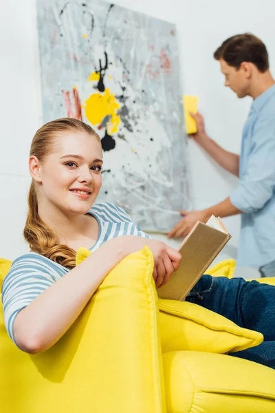 Selective Focus Girl Book Smiling Camera Boyfriend Cleaning Painting Living — Stock Photo, Image