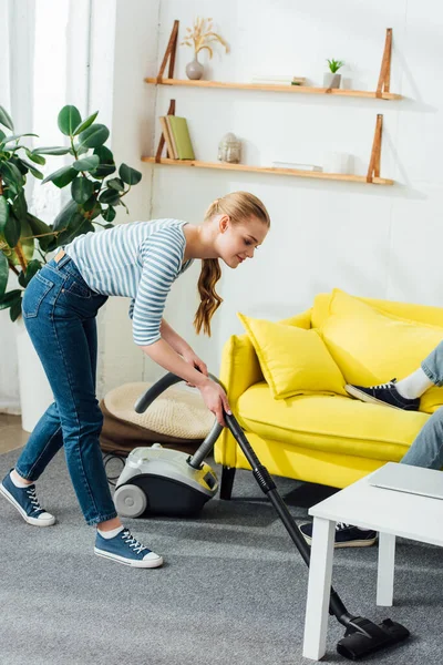 Seitenansicht Frau Putzt Teppich Mit Staubsauger Neben Mann Auf Couch — Stockfoto