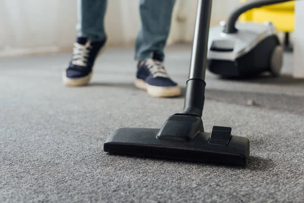 Cropped view of man cleaning carpet with vacuum cleaner at home