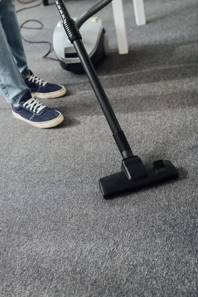 Cropped view of man cleaning carpet in living room with vacuum cleaner