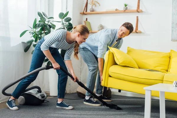 Pandangan Samping Dari Wanita Tersenyum Membersihkan Karpet Dengan Vacuum Cleaner — Stok Foto