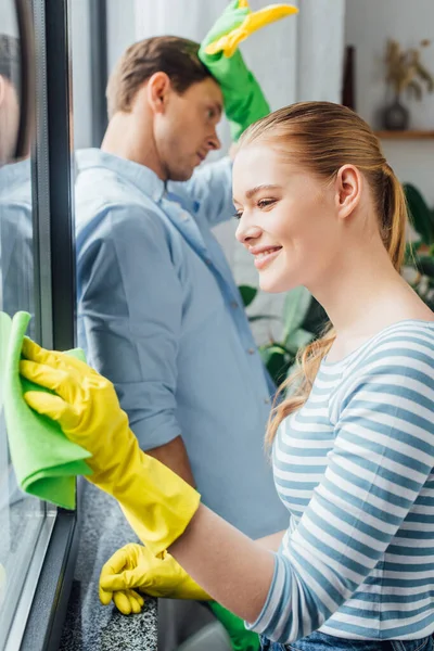 Enfoque Selectivo Chica Sonriente Ventana Limpieza Cerca Novio Cansado Con — Foto de Stock