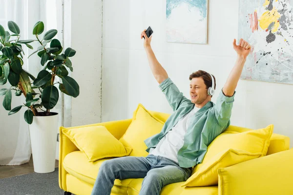 Excited Man Headphones Listening Music Holding Smartphone Couch Home — Stock Photo, Image