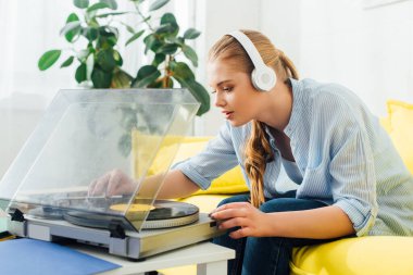 Kulaklıklı çekici bir kızın evdeki kahve masasında pikap kullanmasının yan görüntüsü. 