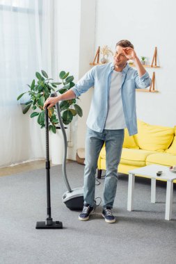 Adam oturma odasında elektrikli süpürge kullanırken gülümsüyor.