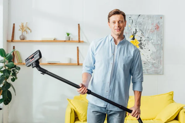 Bonito Homem Sorrindo Para Câmera Enquanto Segurando Escova Aspirador Sala — Fotografia de Stock