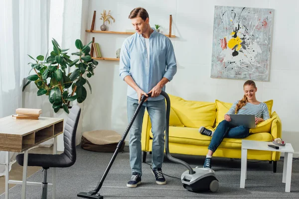 Man Cleaning Carpet Vacuum Cleaner Smiling Girl Using Laptop Couch — Stock Photo, Image