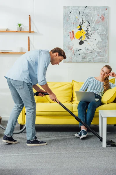 Schöner Mann Putzt Teppich Wohnzimmer Neben Lächelnder Frau Mit Laptop — Stockfoto