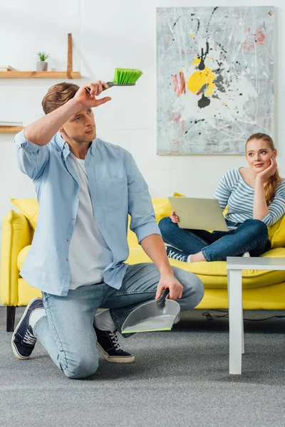 Mujer Con Portátil Mirando Novio Cansado Con Escoba Cucharada Sala — Foto de Stock