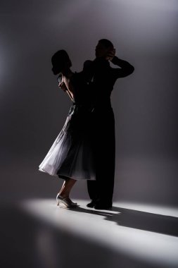 elegant young couple of ballroom dancers in black outfit dancing in dark clipart