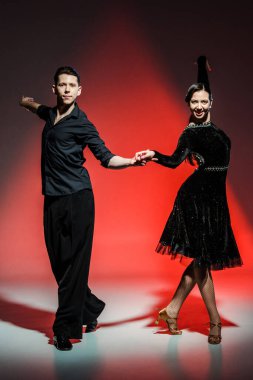 elegant young couple of ballroom dancers in black outfits dancing in red light clipart