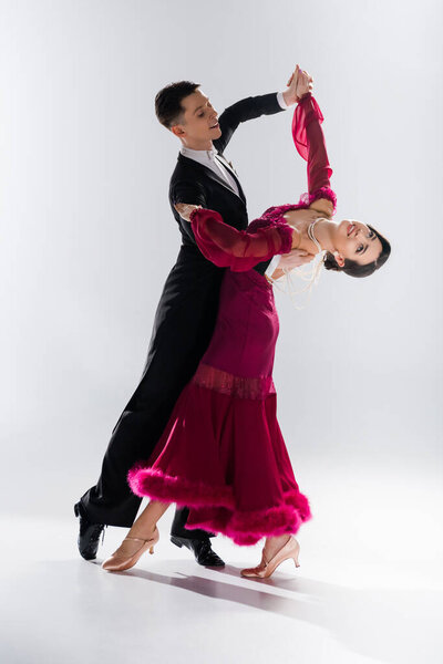 elegant young couple of ballroom dancers in red dress in suit dancing on white