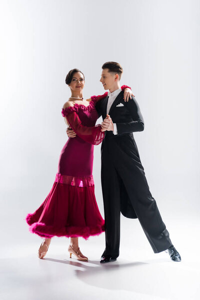 элегантная молодая пара танцовщиц в красном платье в костюме, танцующая на белом
