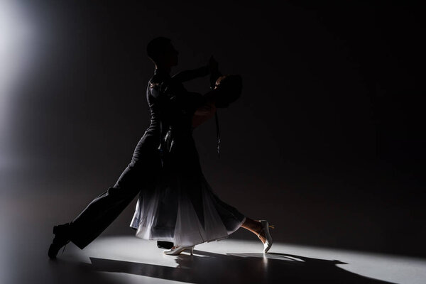 элегантная молодая пара танцовщиц в черном наряде танцует в темноте
