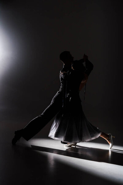 элегантная молодая пара танцовщиц в черном наряде танцует в темноте
