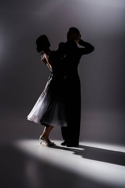 элегантная молодая пара танцовщиц в черном наряде танцует в темноте
