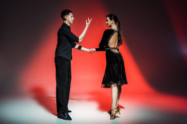 элегантная молодая пара танцовщиц в черных нарядах танцующих в красном свете
