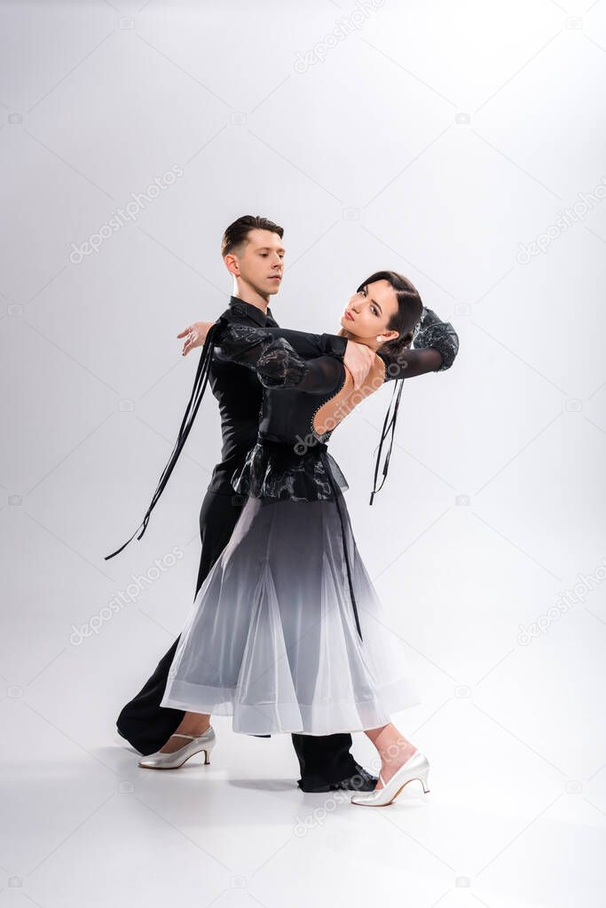 elegant young couple of ballroom dancers in black outfit dancing on white