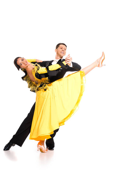 Улыбающаяся элегантная молодая пара танцовщиц в жёлтом платье и чёрном костюме танцующая на белом
