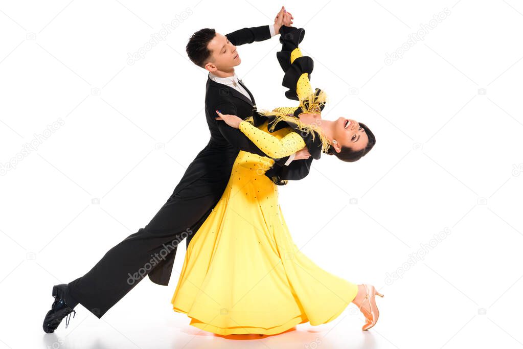 elegant young couple of ballroom dancers in yellow dress and black suit dancing on white